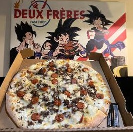 Pizza chorizo dans sa boîte devant la fresque du restaurant